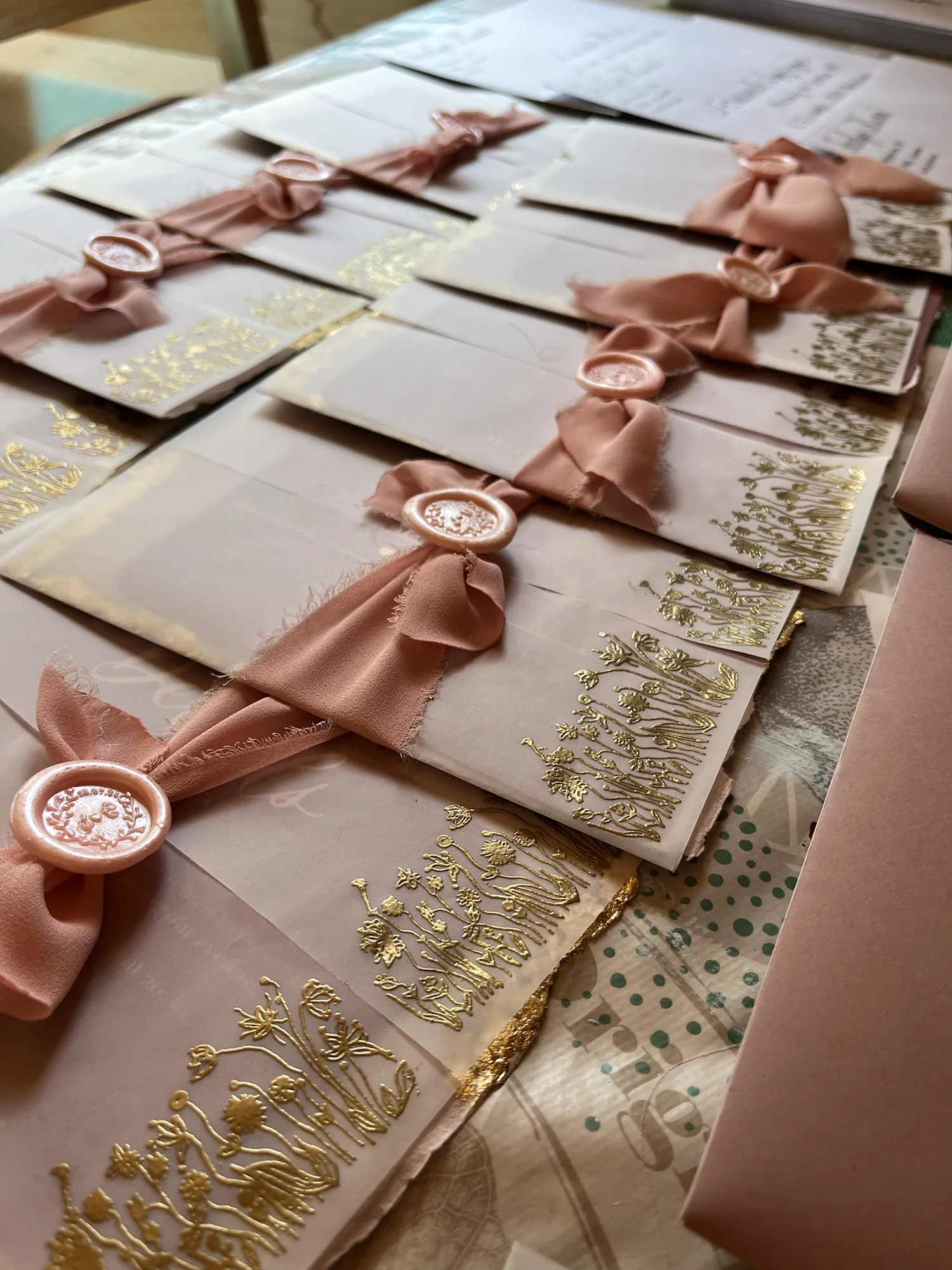 Blush hand-lettered envelopes finished with silk ribbon, wax seals and gold botanical details