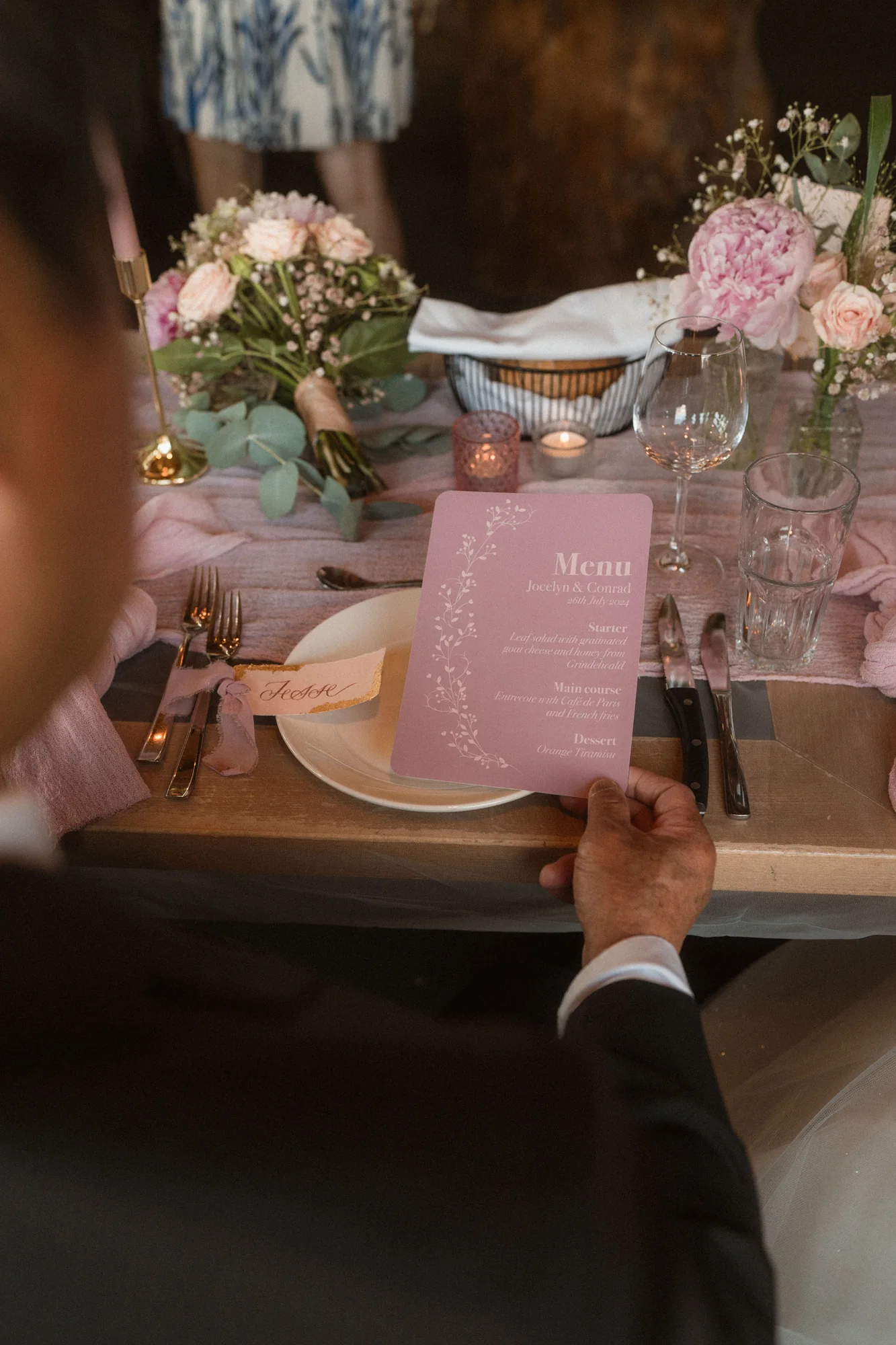 Guest holding a blush wedding menu at a flower-filled place setting
