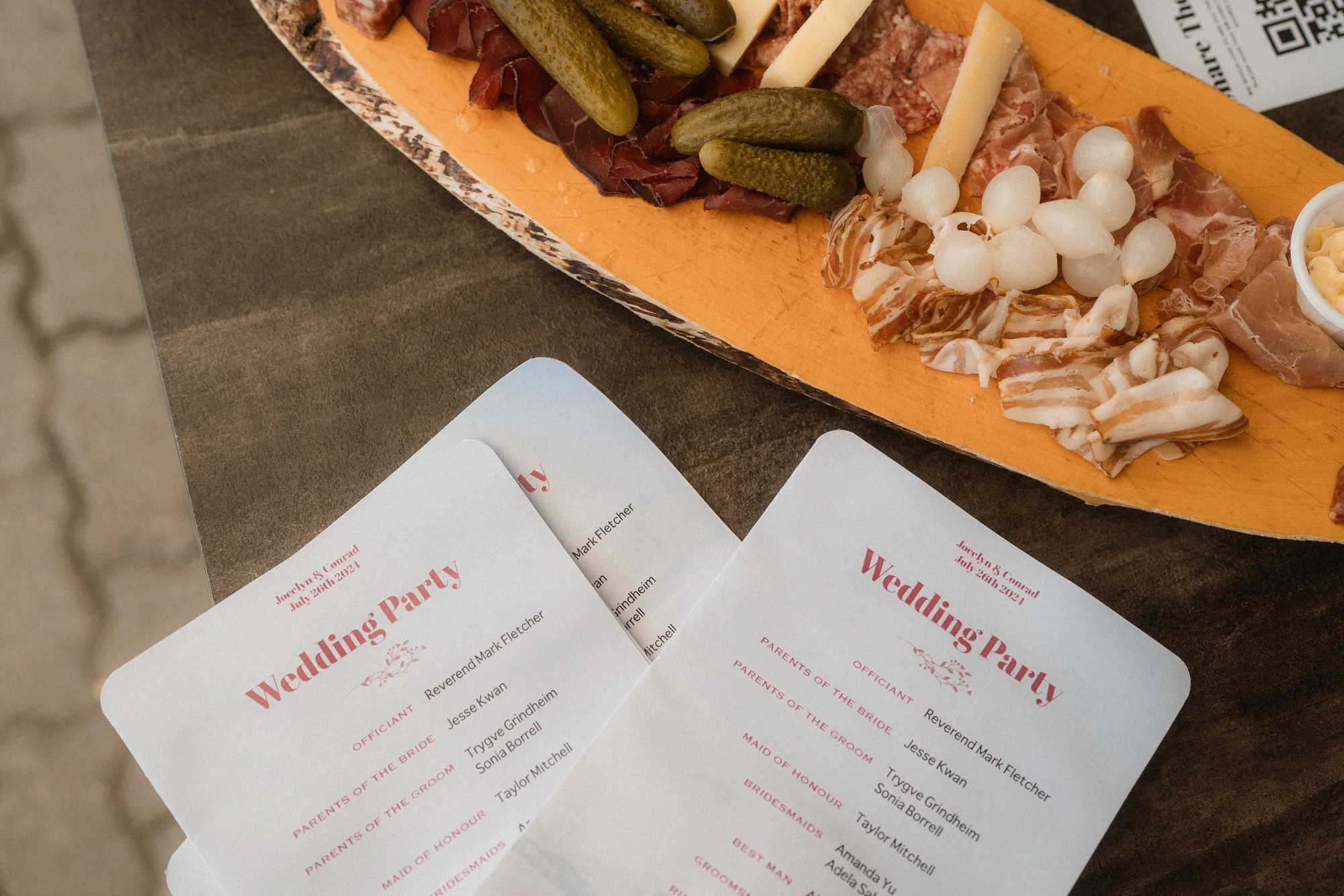 Printed wedding party programmes arranged beside a charcuterie board