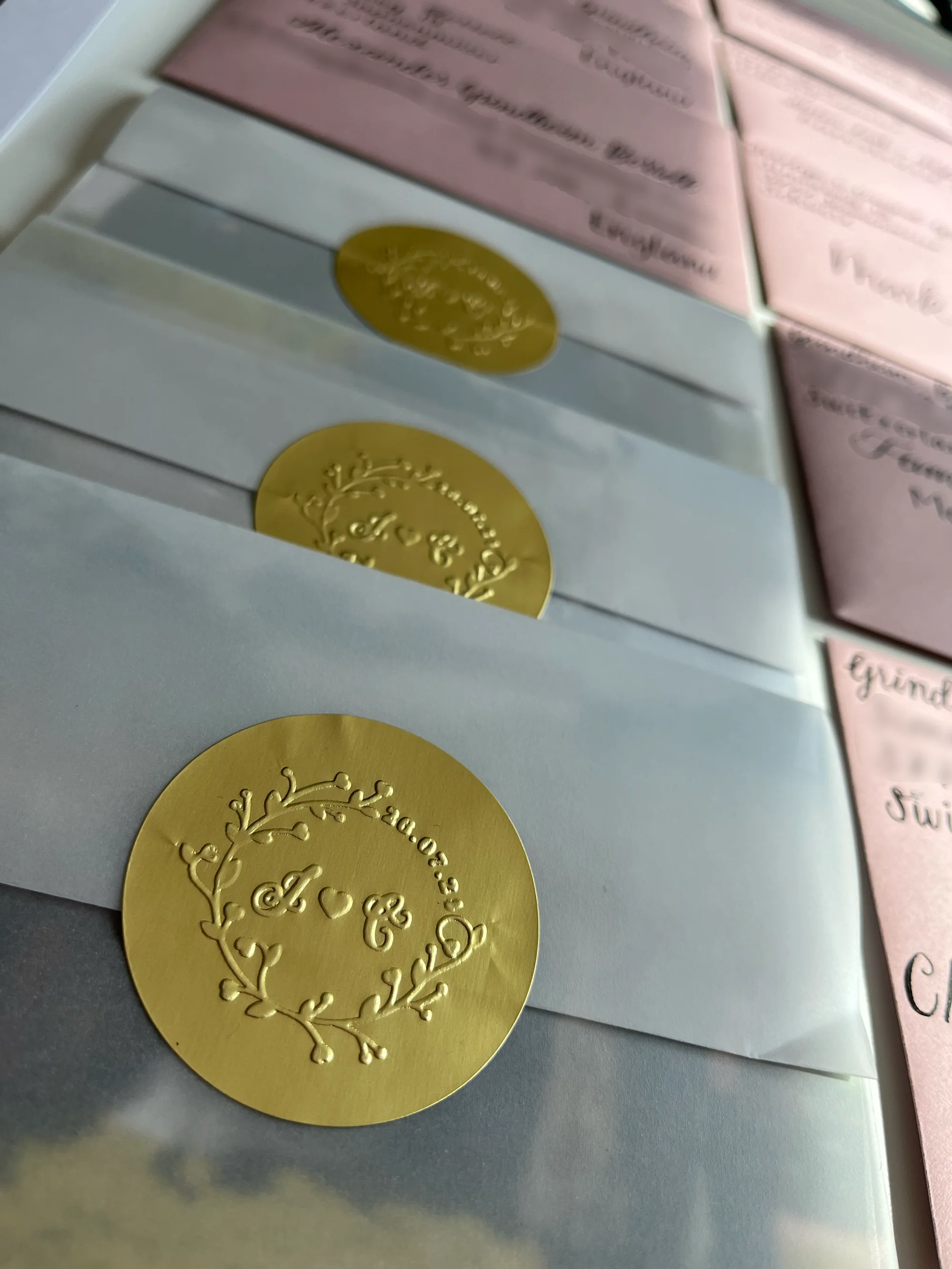 White envelopes sealed with gold custom insignia stickers beside hand-lettered blush envelopes